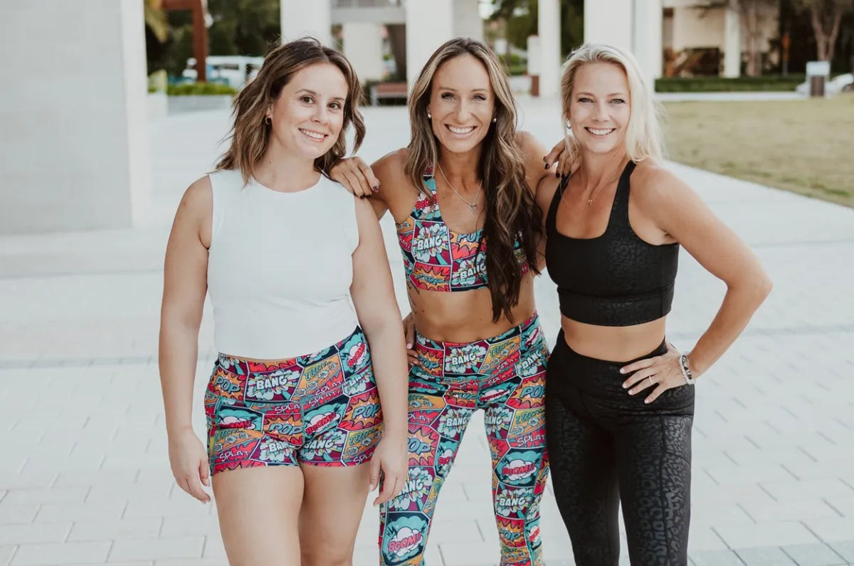 Three women in bright CVG shorts and one in black leggings styling summer outfits with leggings in bold, supportive looks