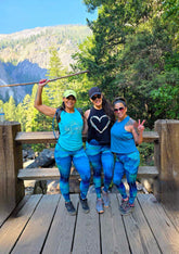 Three women posing on a wooden platform with a mountainous background
