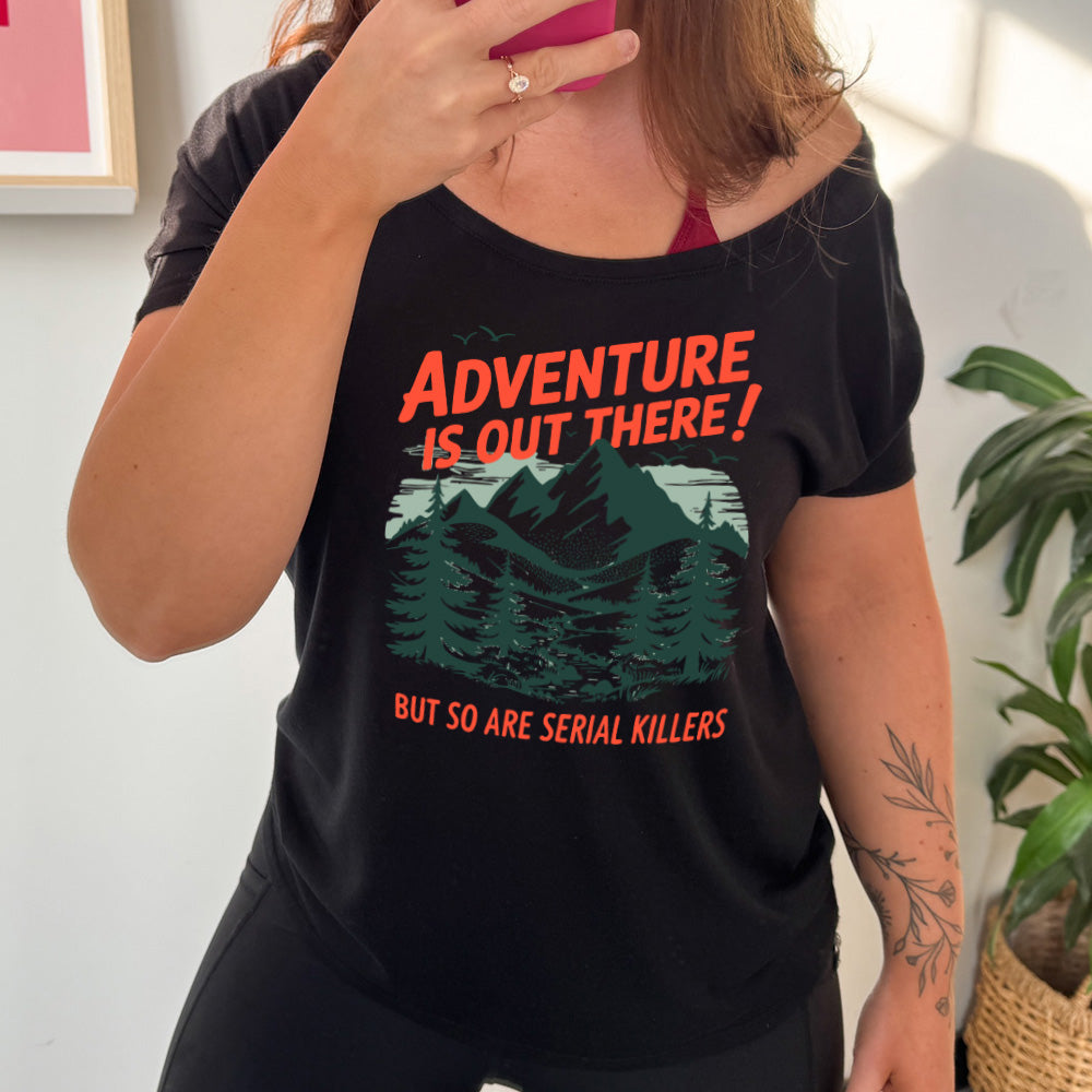 black slouchy tee with the words "adventure is out there! but so are serial killers" on it, with the graphic of mountains and woods and birds flying