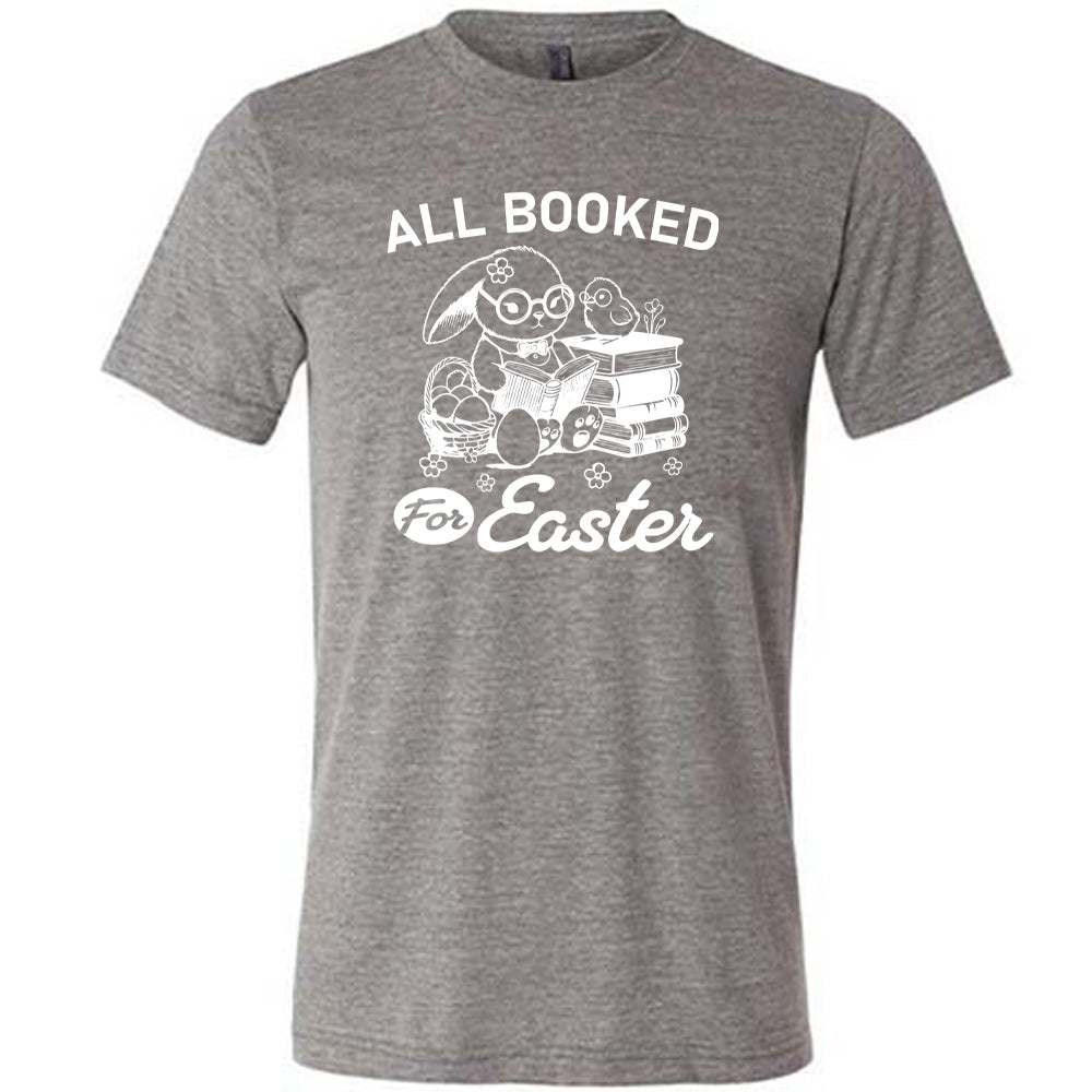 grey unisex tee with the words "all booked for Easter" on it, and the graphic of a bunny wearing glasses and a bowtie, reading a book, next to a stack of books (with a bird wearing glasses on top of it) on one side, and a basket of eggs on the other side