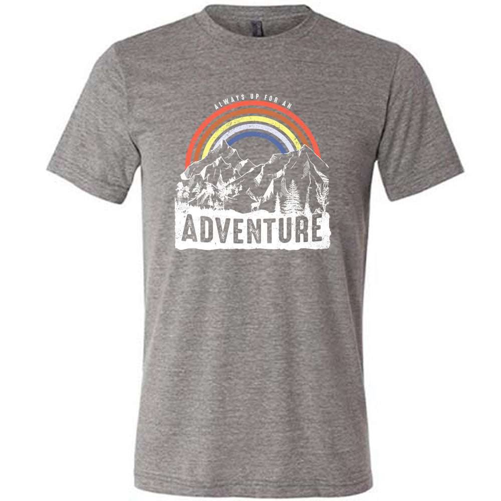 Grey colored shirt with a rainbow over mountains graphic on it that says "Always Up For An Adventure"