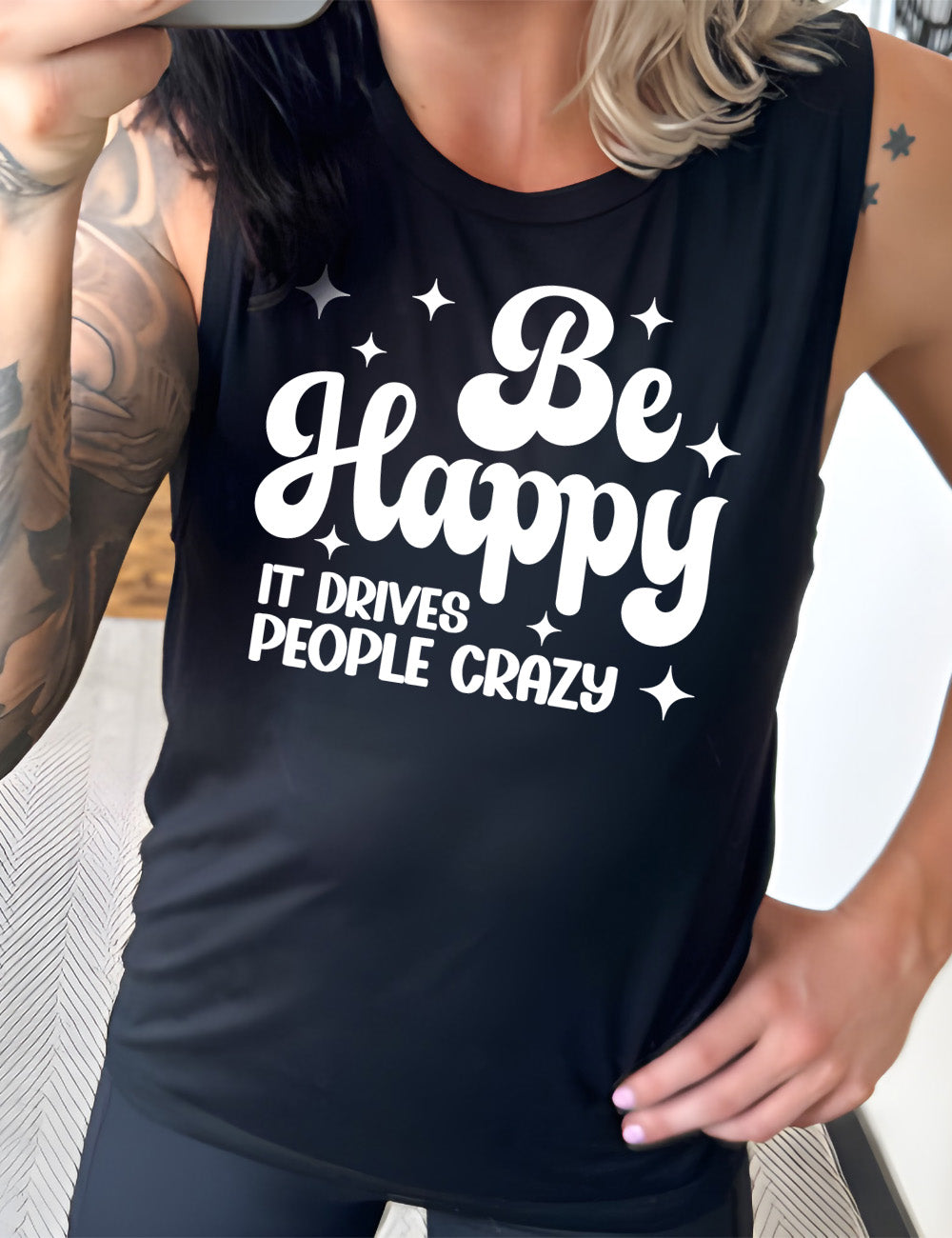 black muscle tank with the words "be happy it drives people crazy" on it, with a number of stars around