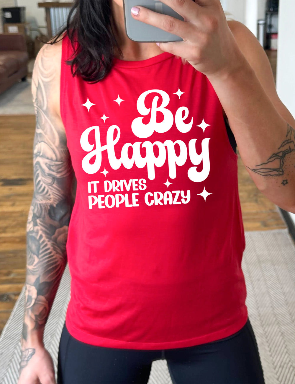 red muscle tank with the words "be happy it drives people crazy" on it, with a number of stars around