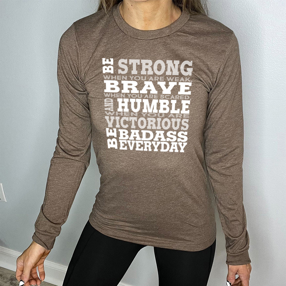heather brown long sleeve with the words "Be STRONG when you are weak, BRAVE when you are scared, and HUMBLE when you are victorious be badass everyday" in white lettering