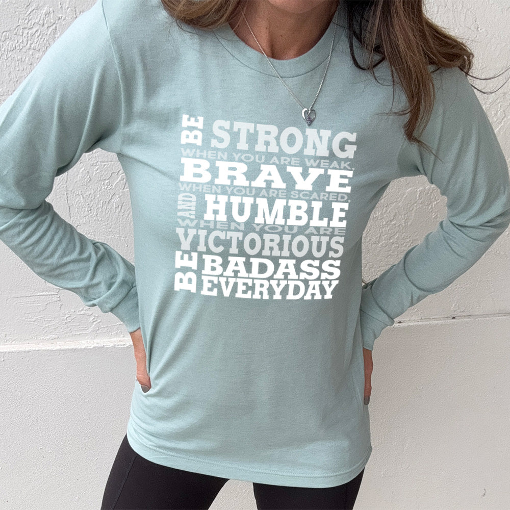 heather dusty blue long sleeve with the words "Be STRONG when you are weak, BRAVE when you are scared, and HUMBLE when you are victorious be badass everyday" in white lettering