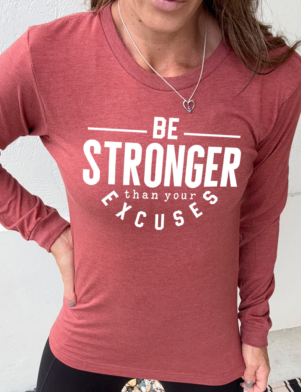 heather clay long sleeve tee with words on it saying "be STRONGER than your excuses", with lines in front and after the word "be", the word "stronger" in the largest font, and the word "excuses" arching