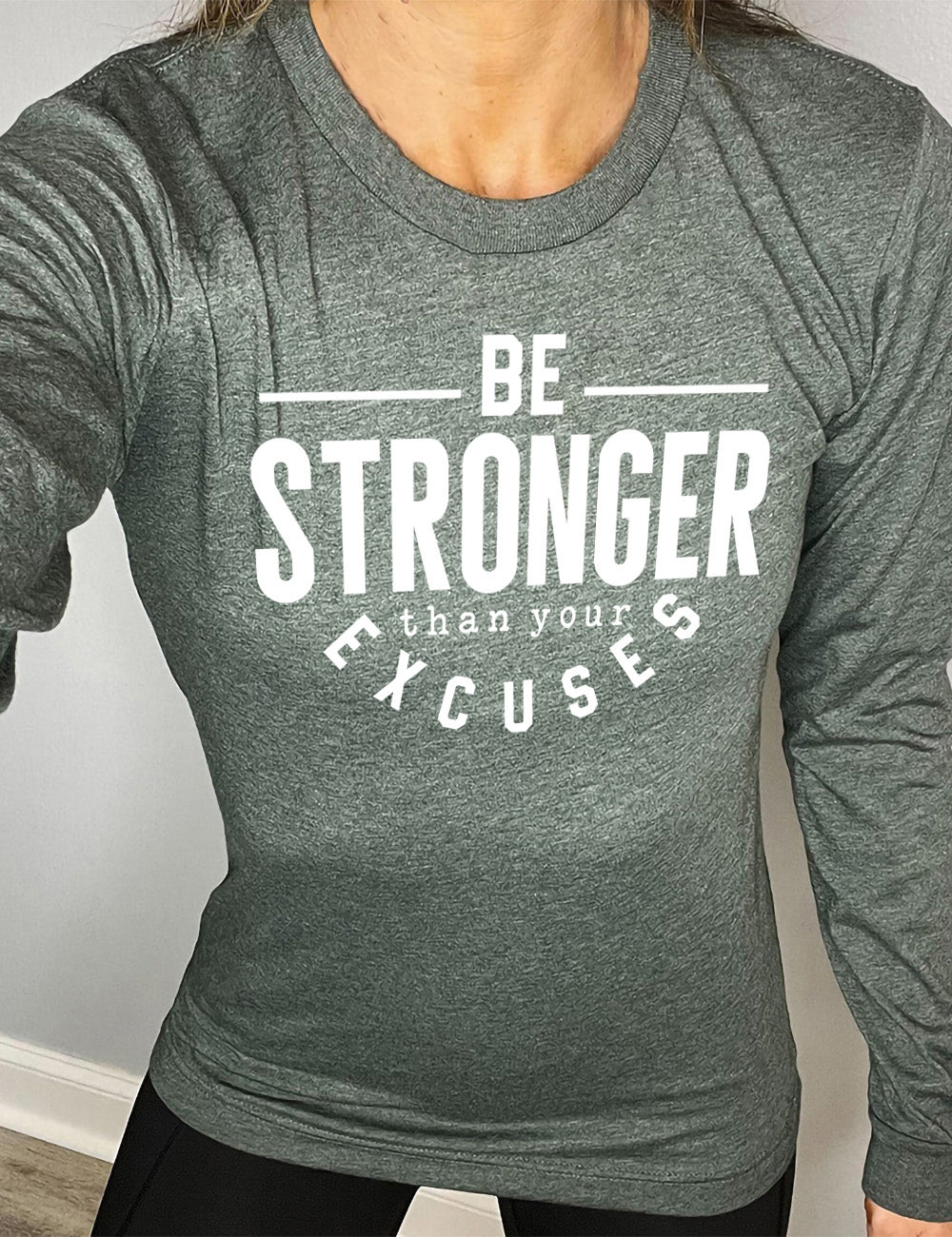 heather forest long sleeve tee with words on it saying "be STRONGER than your excuses", with lines in front and after the word "be", the word "stronger" in the largest font, and the word "excuses" arching