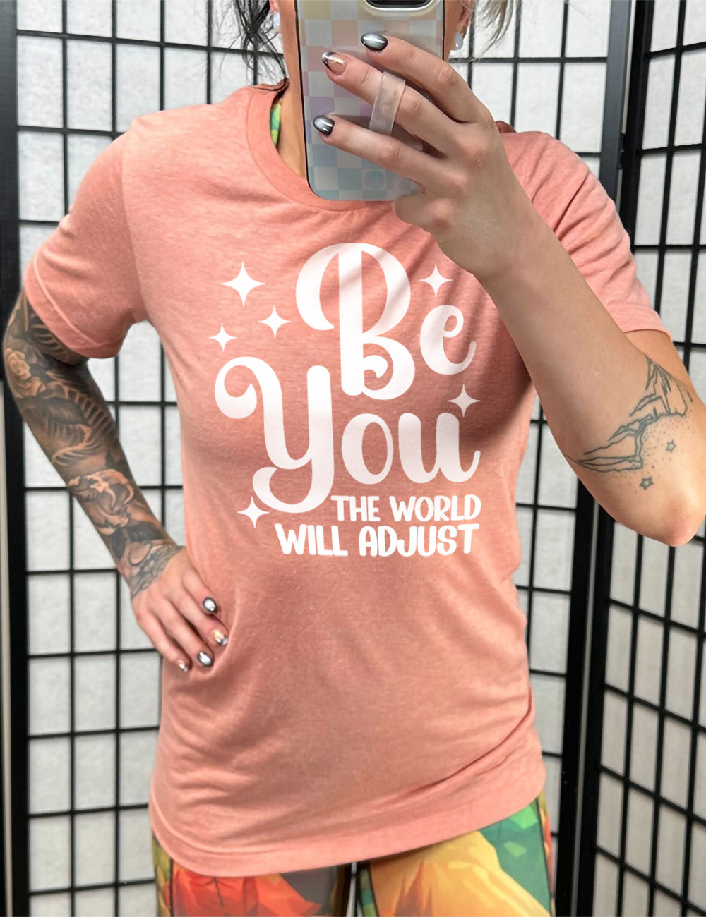 sunset unisex tee with the words "be you" in big letters, surrounded by a few little stars, followed by the words "the world will adjust" underneath