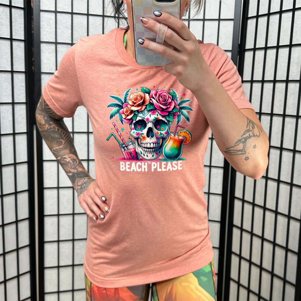 Model wearing sunset colored shirt with a flowery skull and drinks graphic on it that says "Beach Please"