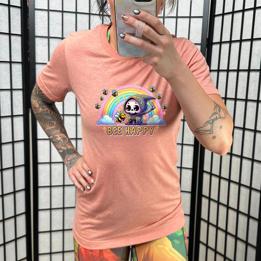 Sunset colored shirt with a grim reaper & bee in front of a rainbow graphic on it that says "Bee Happy"