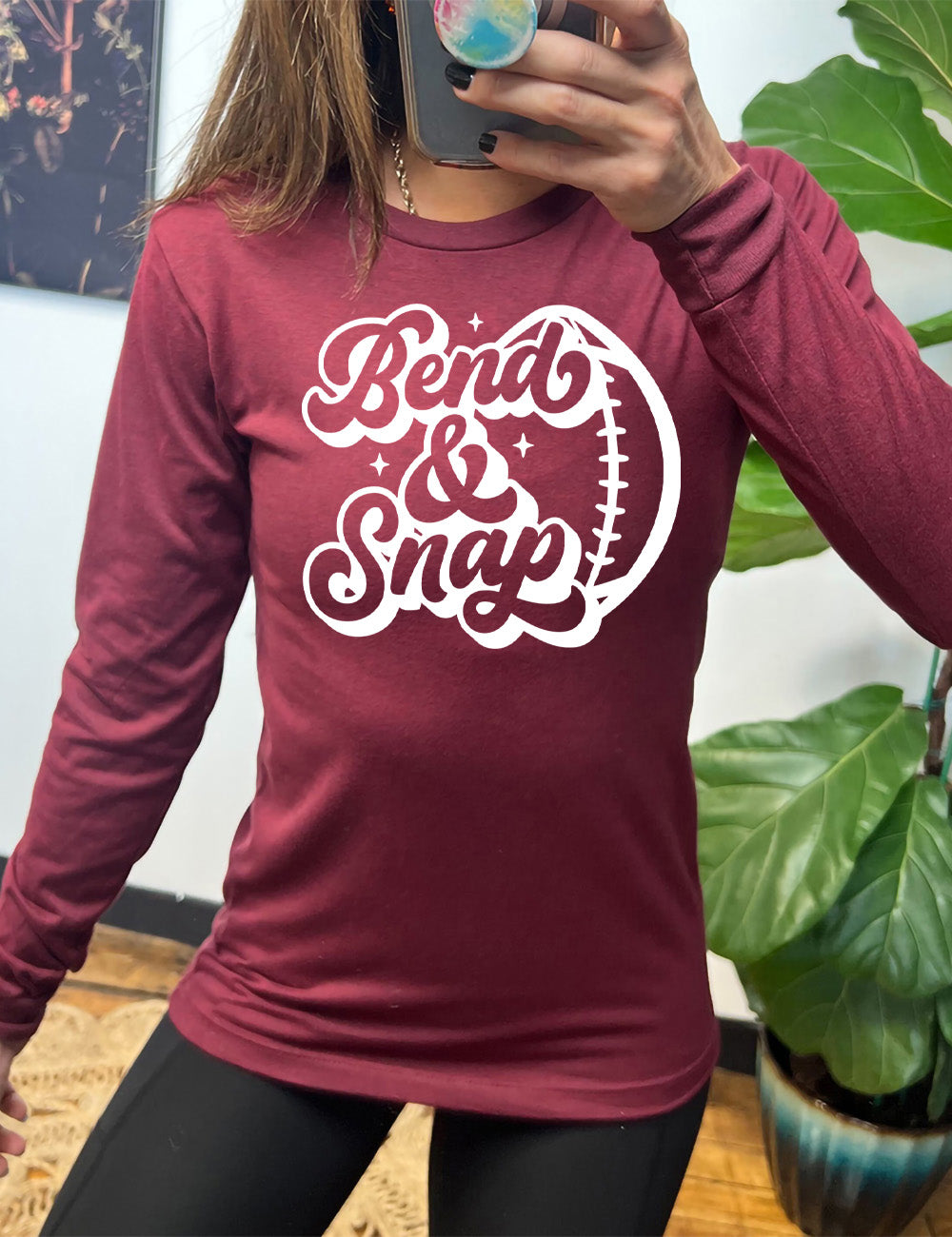 heather cardinal long sleeve tee with the words in cursive saying "Bend & Snap" with the outline graphic of a football slightly underneath