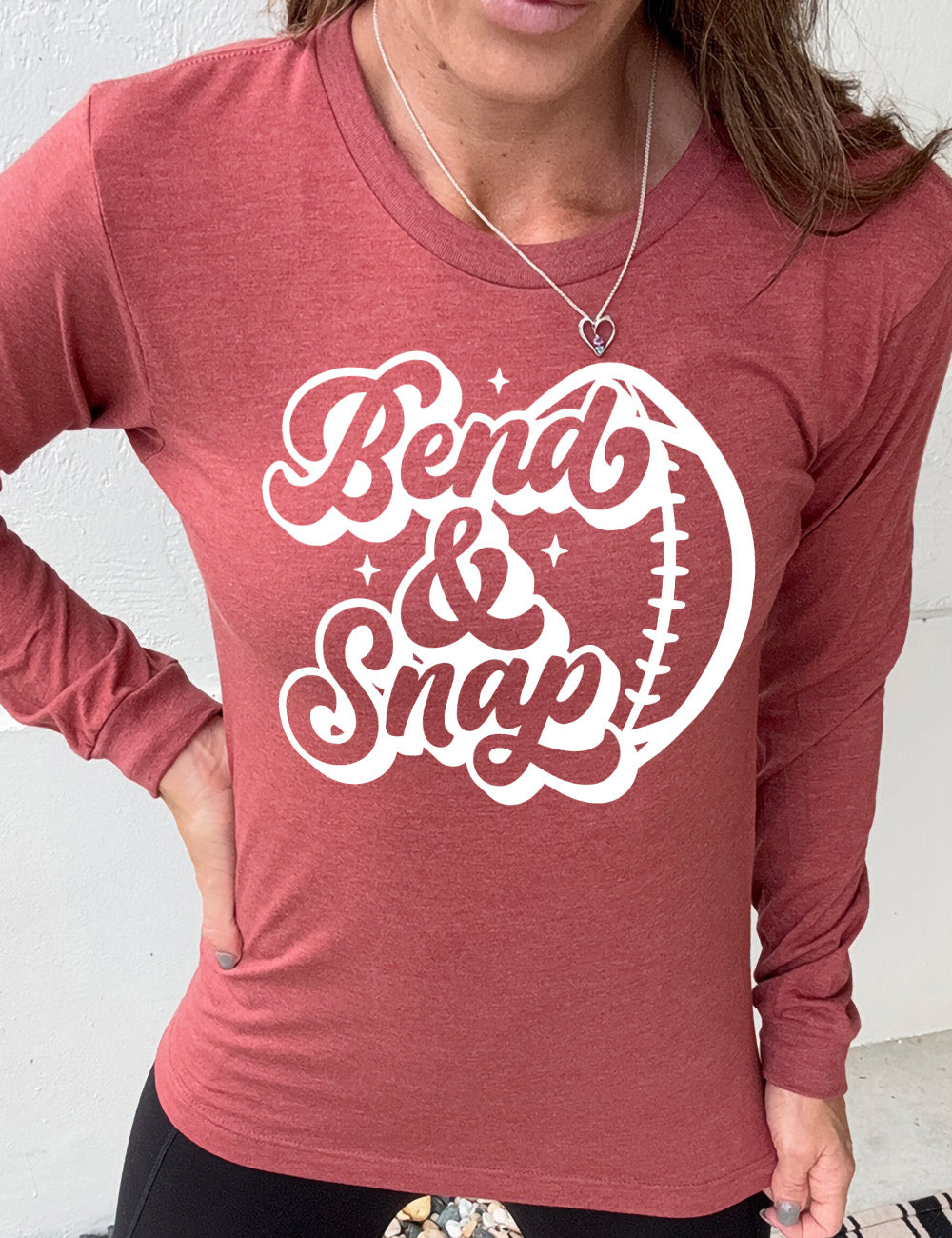 heather clay long sleeve tee with the words in cursive saying "Bend & Snap" with the outline graphic of a football slightly underneath