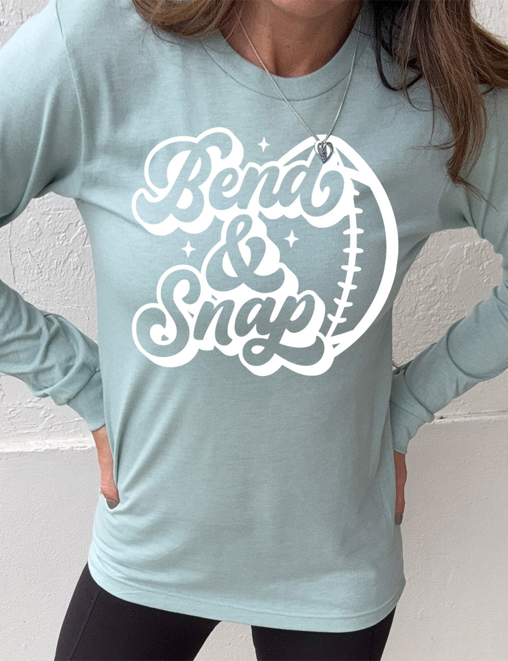 heather dusty blue long sleeve tee with the words in cursive saying "Bend & Snap" with the outline graphic of a football slightly underneath