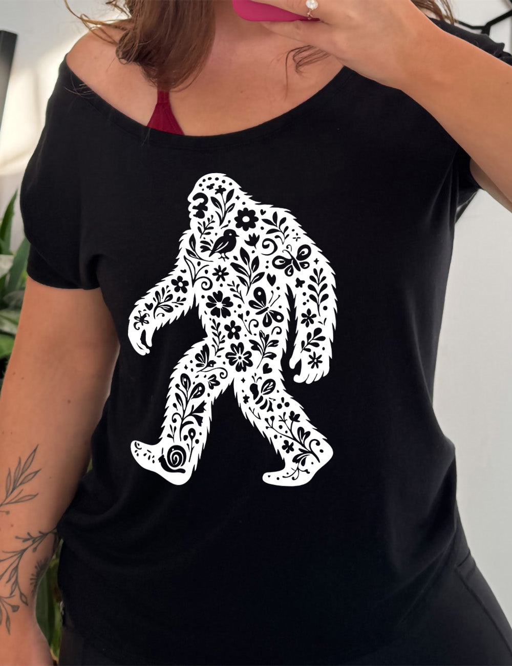 black slouchy tee with the graphic white cutout of bigfoot, which is overlayed with black flowers, plants, birds, bees, snails, and butterflies