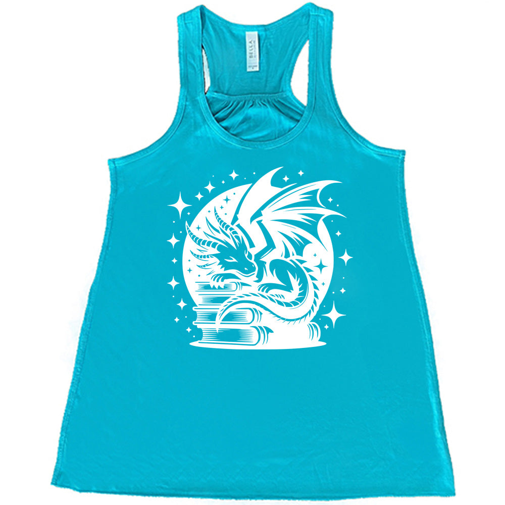teal racerback tank with the graphic of a dragon resting on a stack of books, in front of a full moon, with many stars around