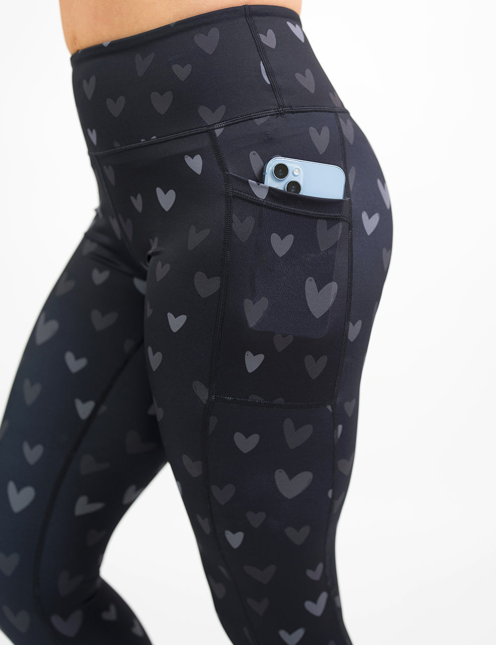 close up of the black leggings with light and dark grey hearts with a phone in its pocket