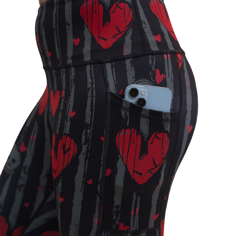 close up of the red heart and gray skulls against a black and grey striped background leggings with a phone in its pocket