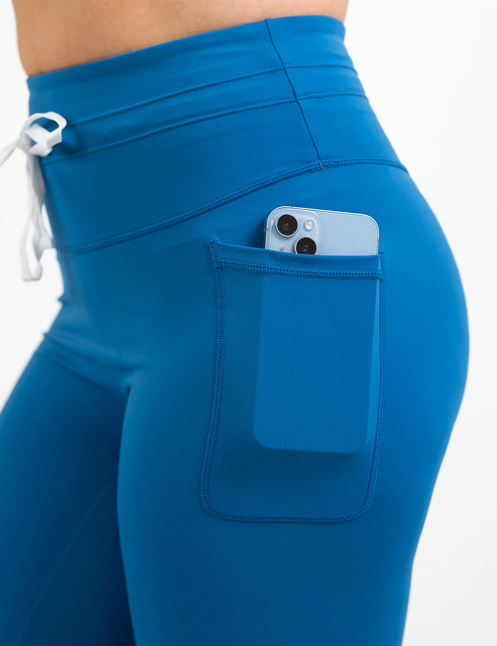 close up of the blue omni leggings with white drawstrings and a phone in its pocket