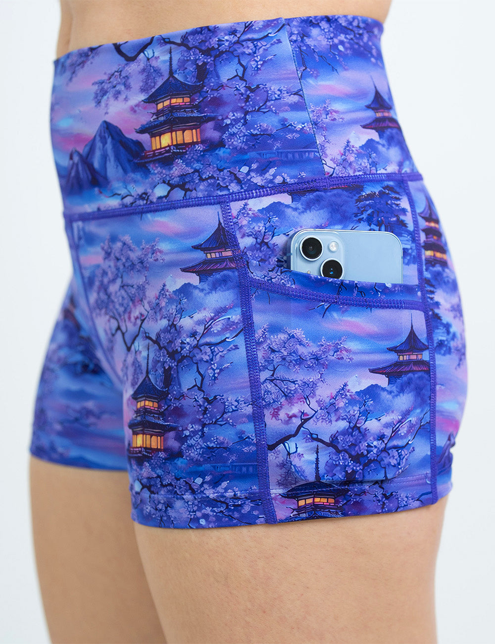 close up of the 2.5 inch blue and lavender shorts with traditional pagodas and blooming cherry trees holding a phone in its pocket