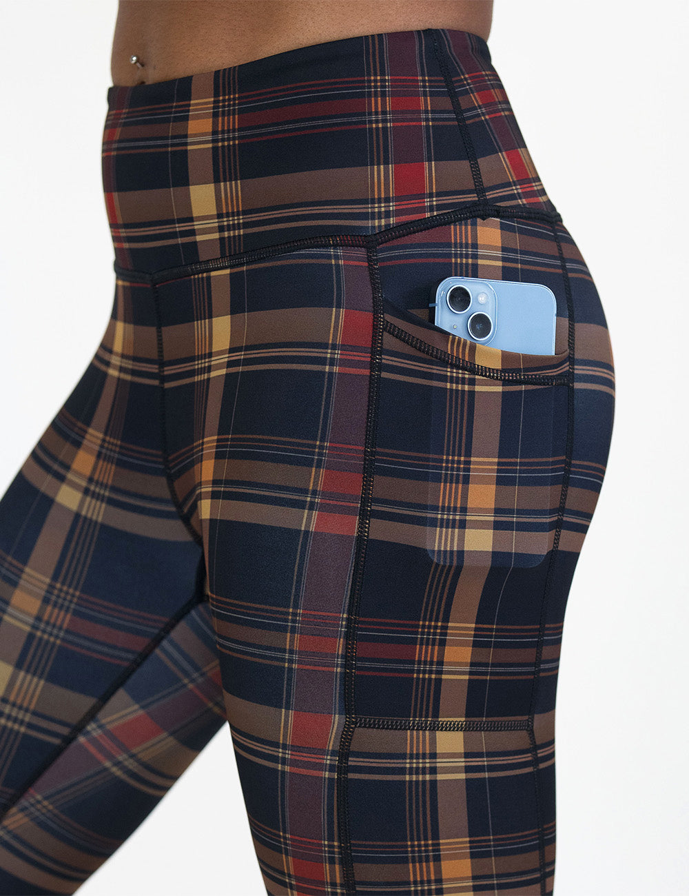 close up of the red, black, and gold plaid leggings with a phone in its pocket