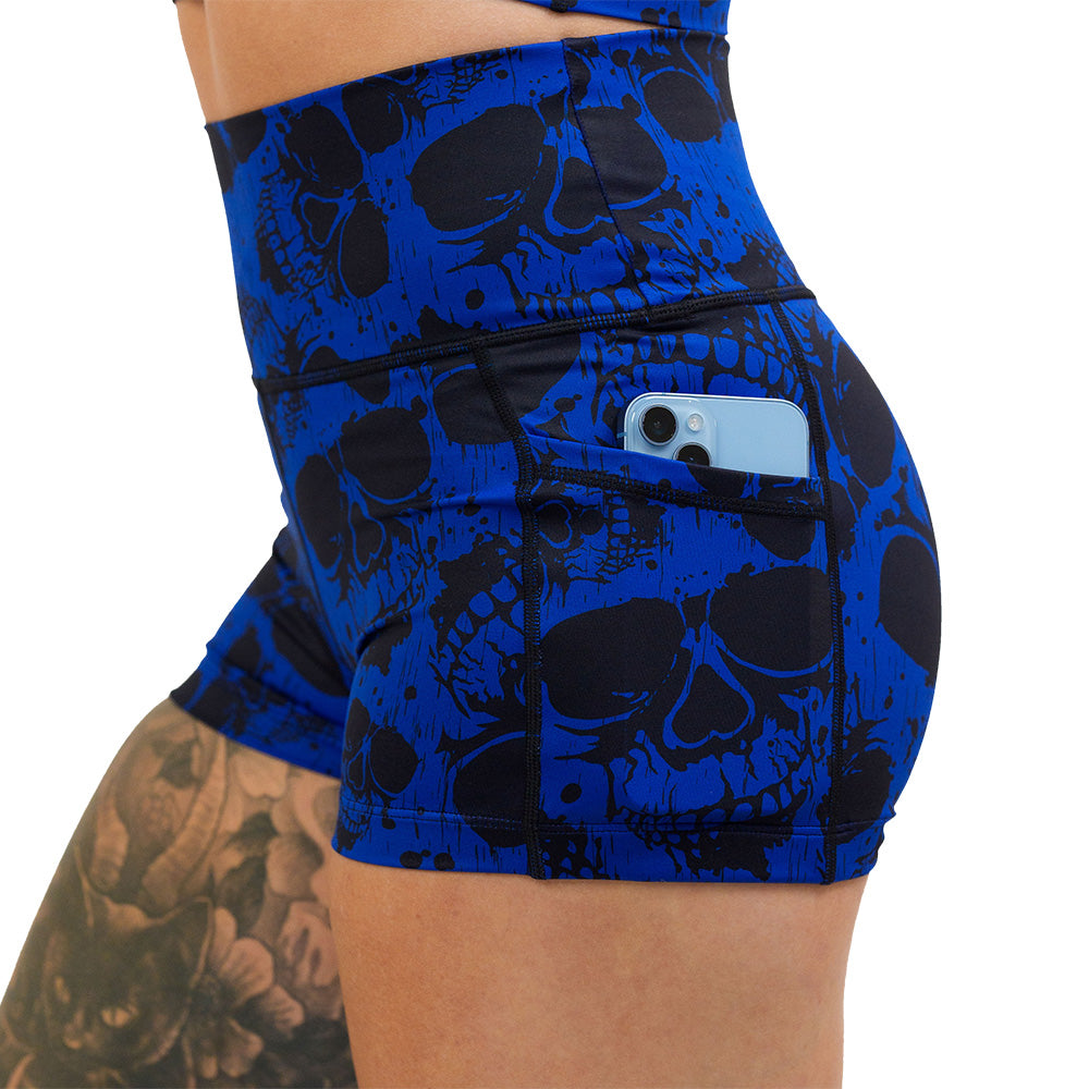 close up of the 2.5 inch dark skulls against a blue background pattern shorts with a phone in the pocket