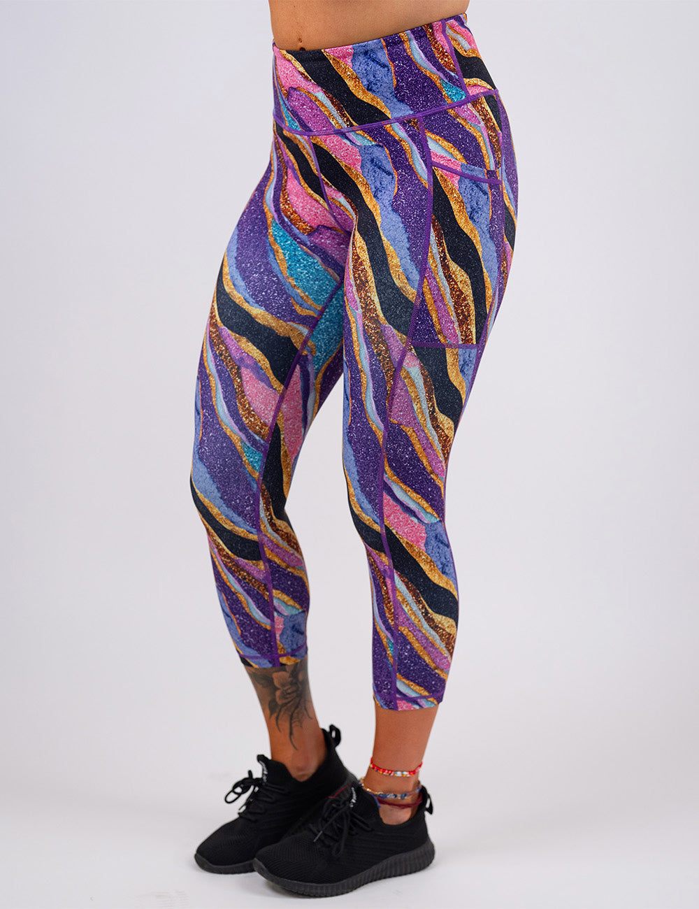 model wearing the purple, gold, black, blue, and pink abstract stripes capri leggings against a white background