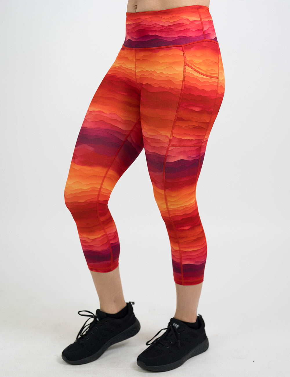 front of the orange, red, and yellow sunset stripes pattern capri leggings against a white background
