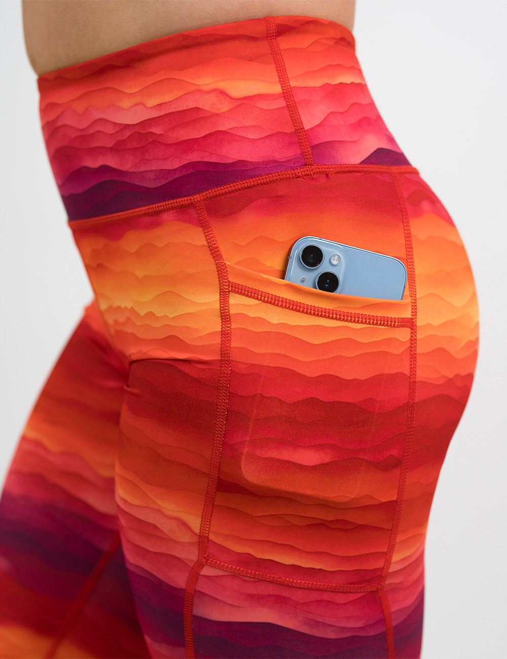 close up of the orange, red, and yellow sunset stripes pattern leggings with a phone in its pocket