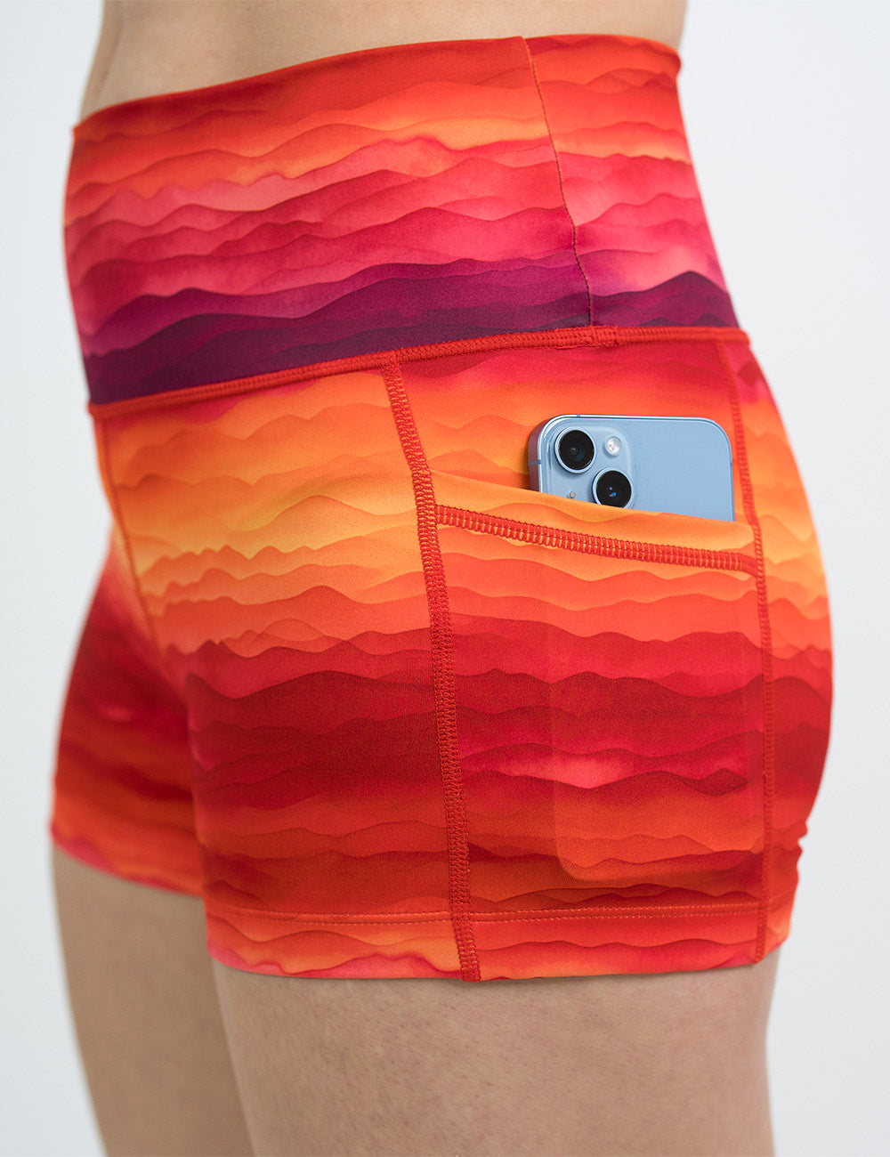 close up of the red, yellow, and orange sunset stripes pattern 2.5 inch shorts with a phone in its pocket
