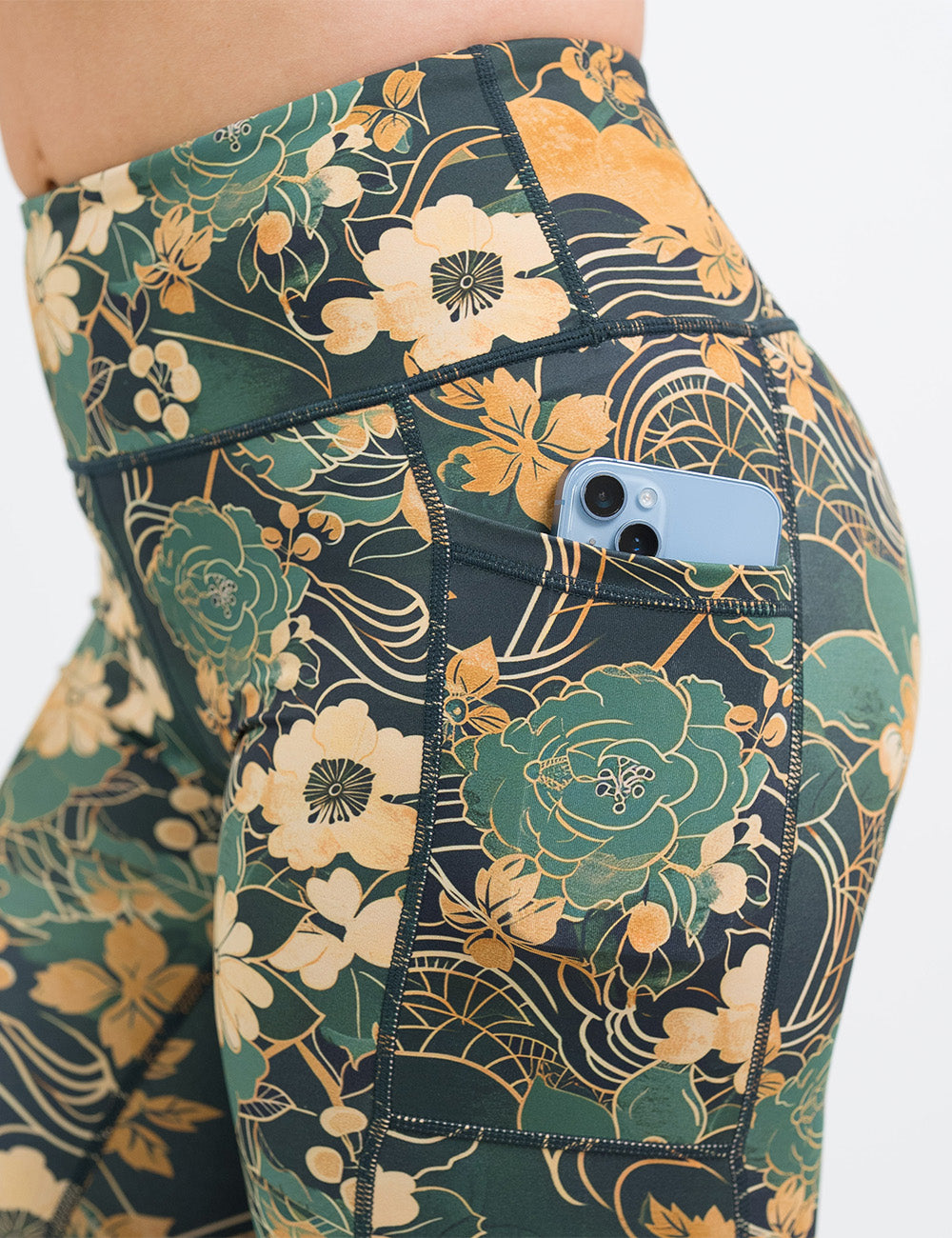close up of the gold and green flowers with gold accents pattern leggings with a phone in its pocket