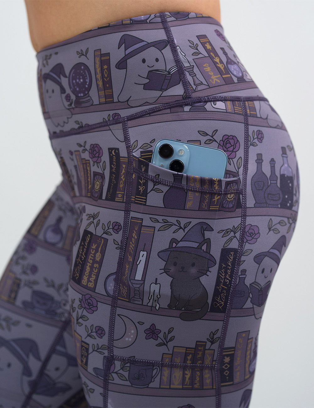 close up of the ghosts and cats book shelves leggings with a phone in its pocket