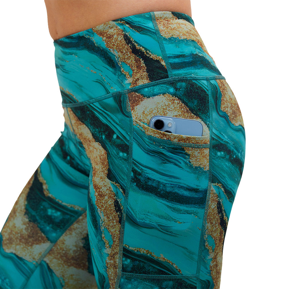 close up of blue ocean with gold streaks patterned leggings with a phone in its pocket