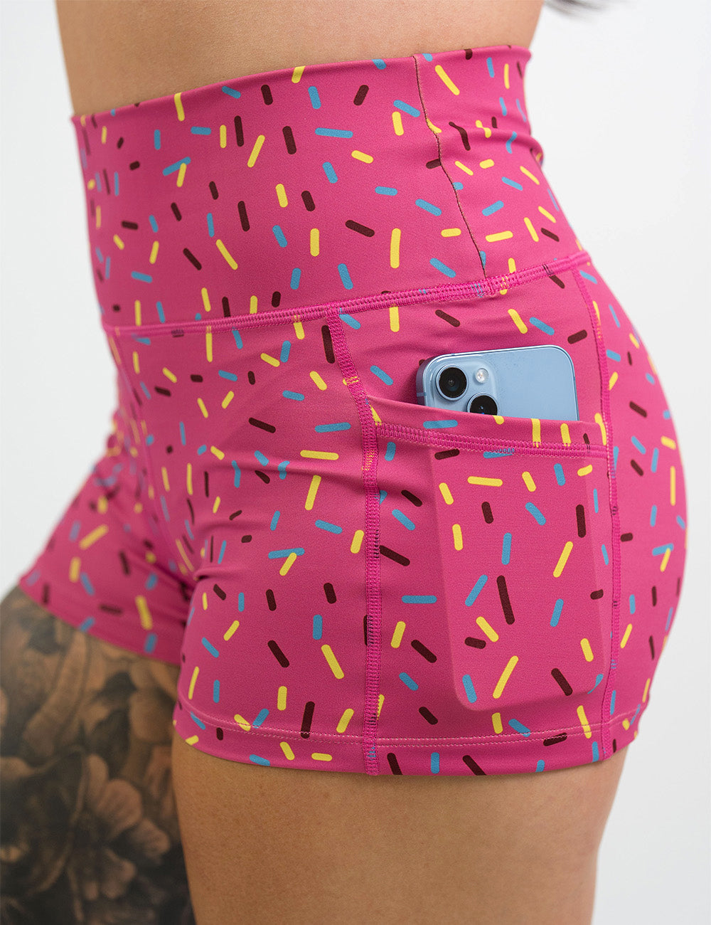 close up of the 2.5 inch pink shorts with a sprinkles pattern holding a phone in its pocket