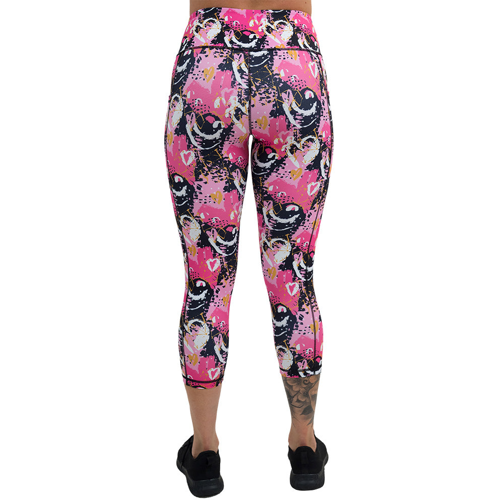 back of white hearts against a bold pink, black, and yellow pattern capri leggings against a white background