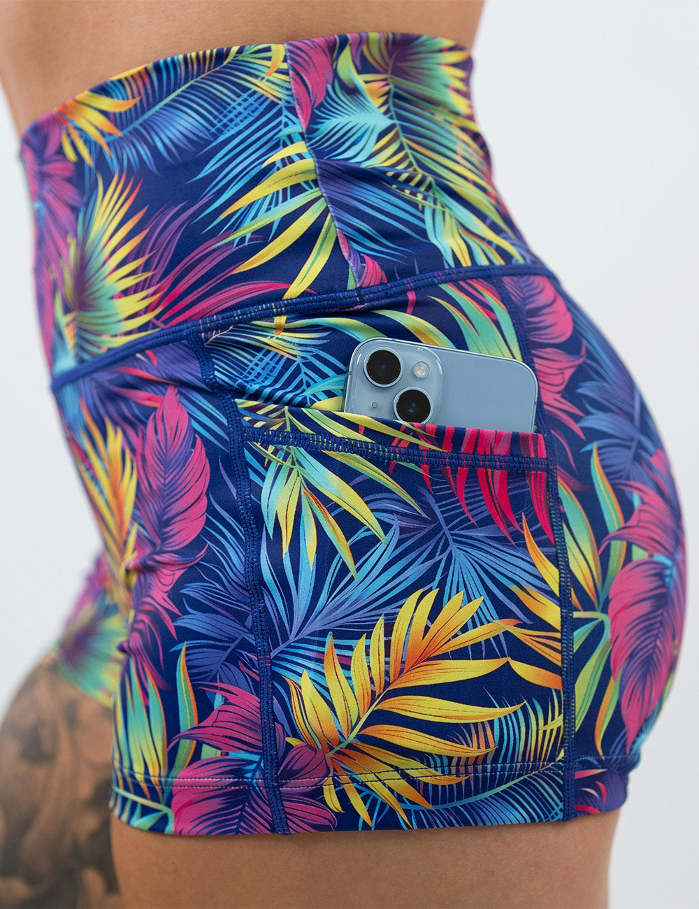 close up of a phone in the pocket of the 2.5 inch vibrant tropical leaves shorts against a white background