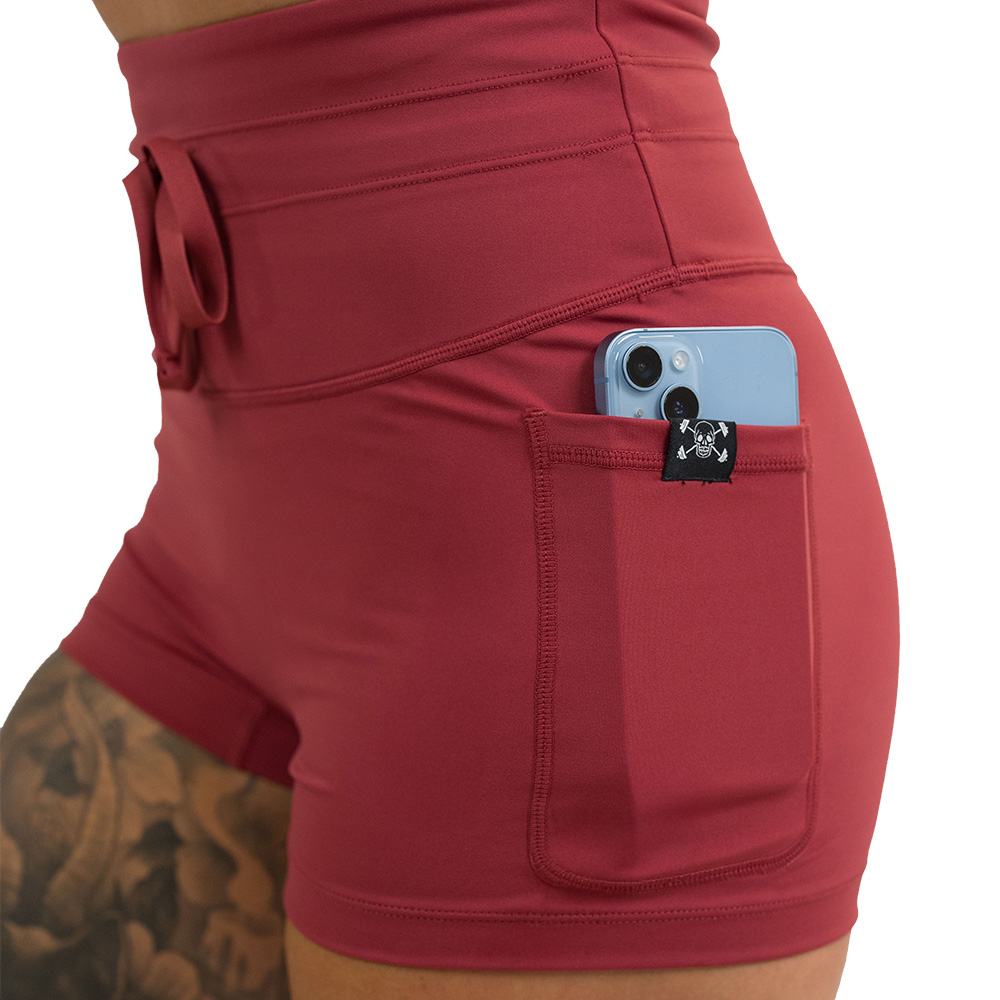 close up of the 2.5 inch omni garnet red shorts with a phone in the pocket against a white background