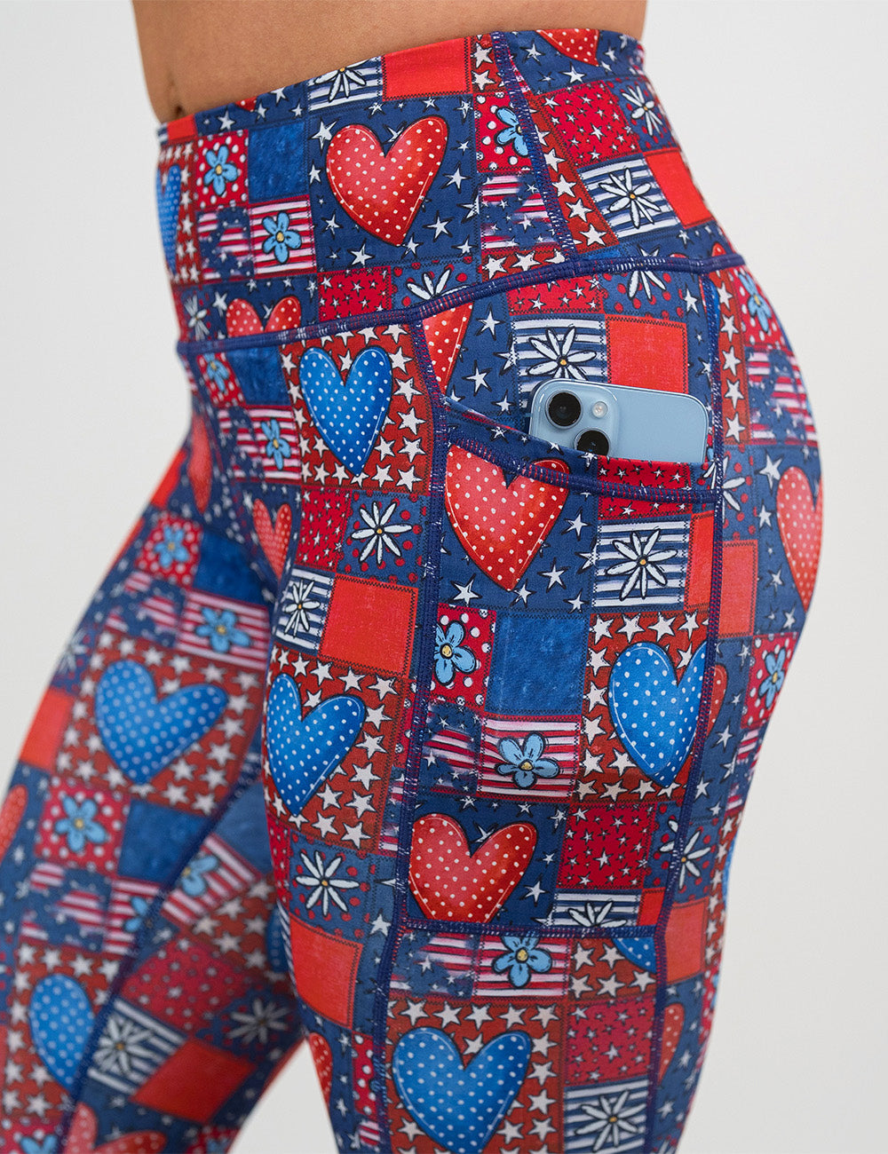 close up of the red white and blue with hearts and flowers patchwork pattern leggings with a phone in its pocket