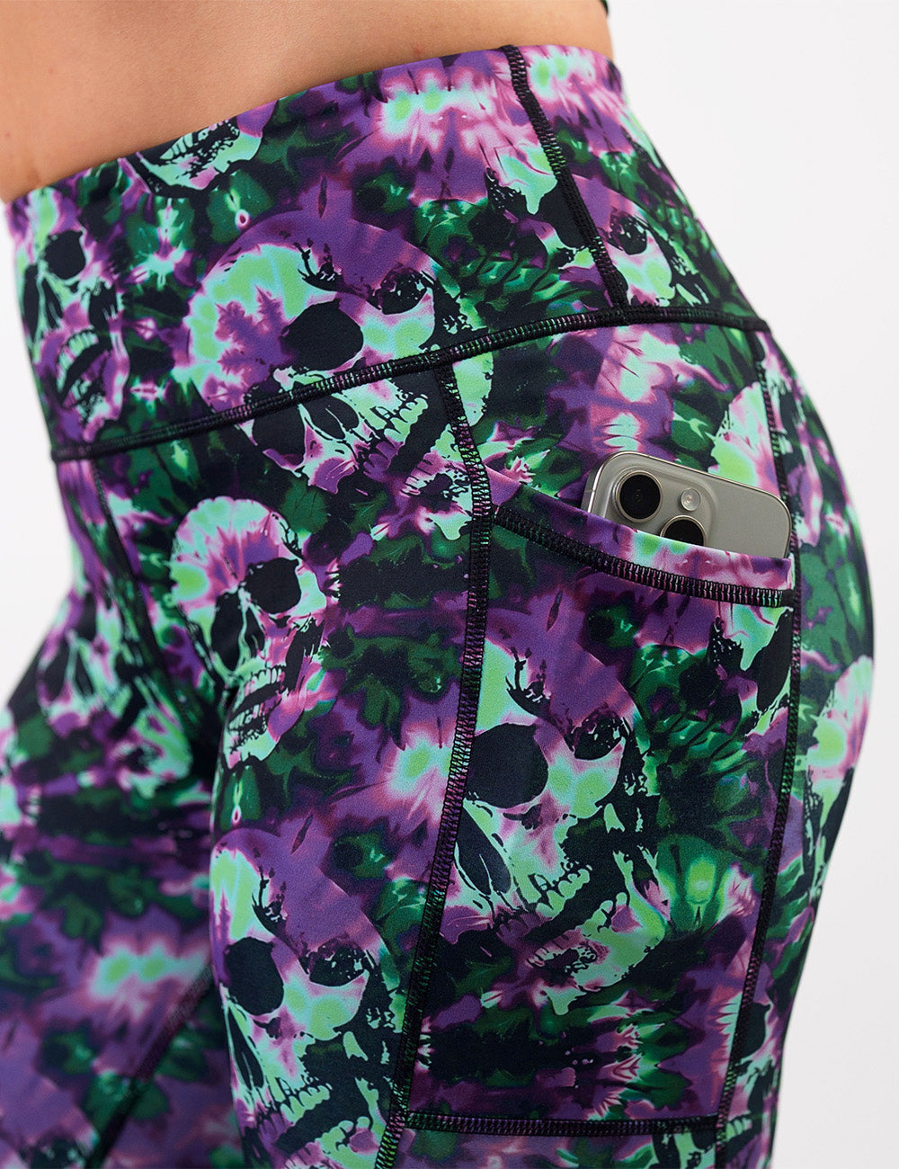 close up of the purple and green tie dye skulls leggings with a phone in its pocket