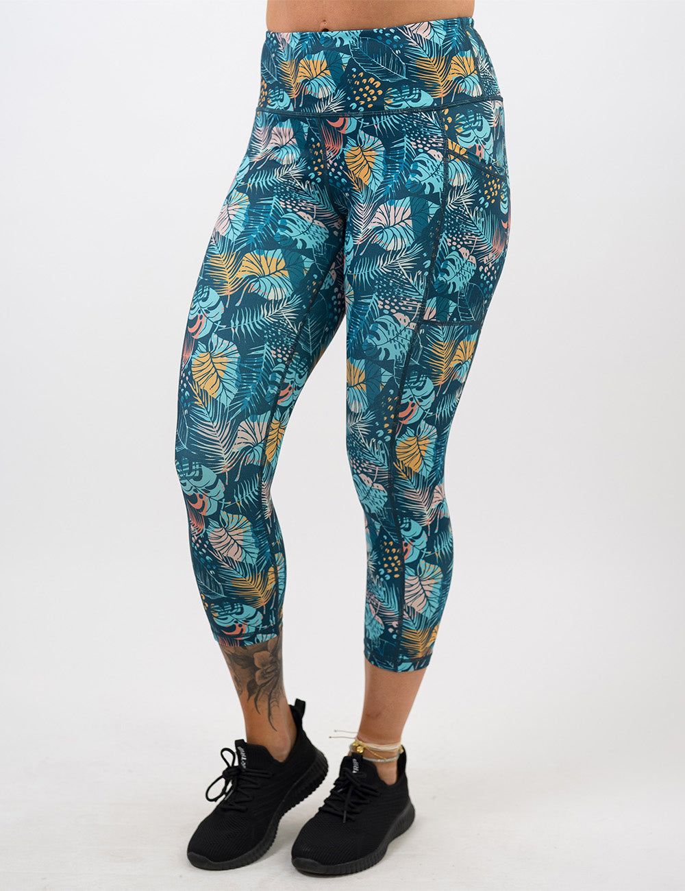 front of the capri blue, pink, yellow, and red tropical leaves leggings against a white background