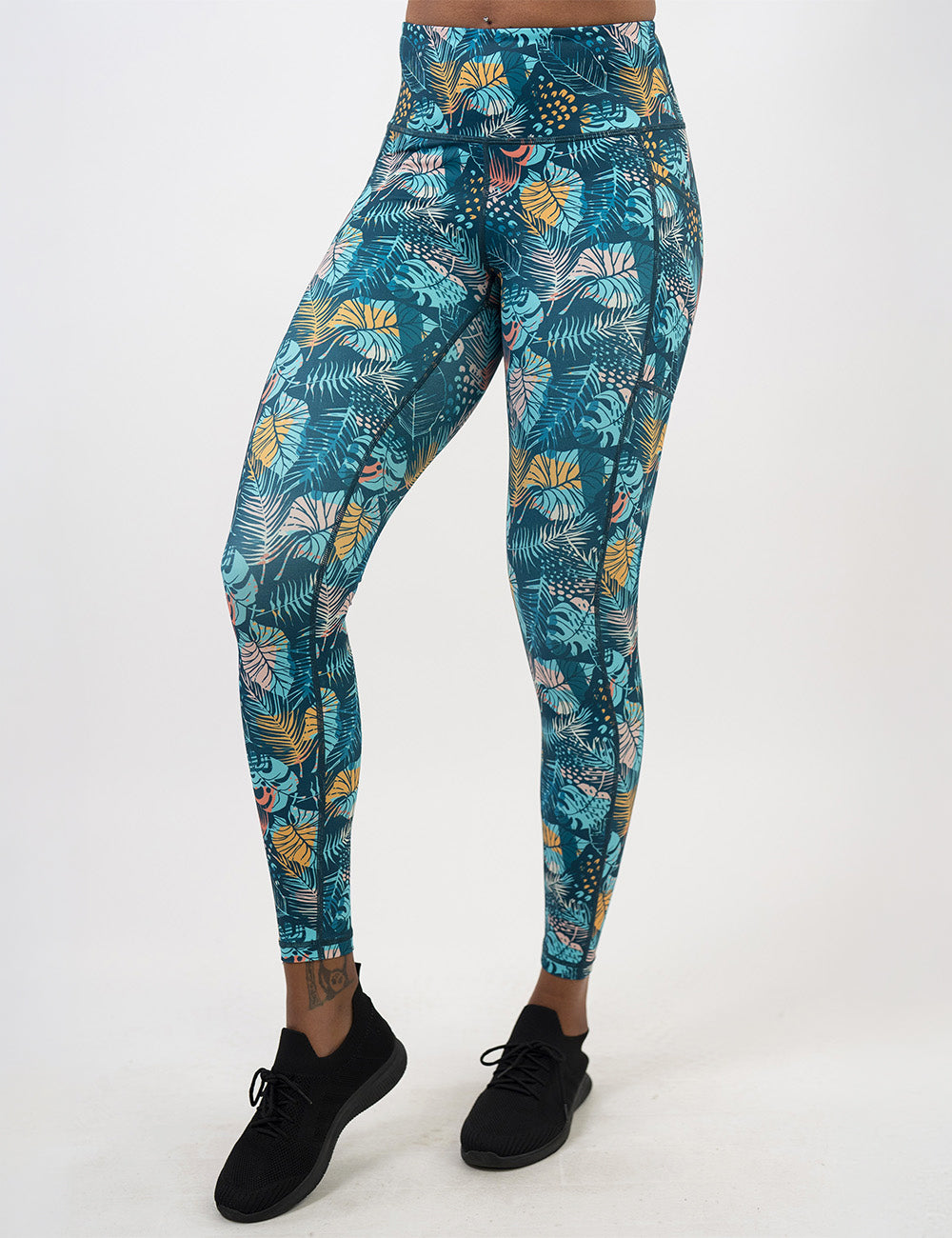 front of the full length blue, pink, yellow, and red tropical leaves leggings against a white background
