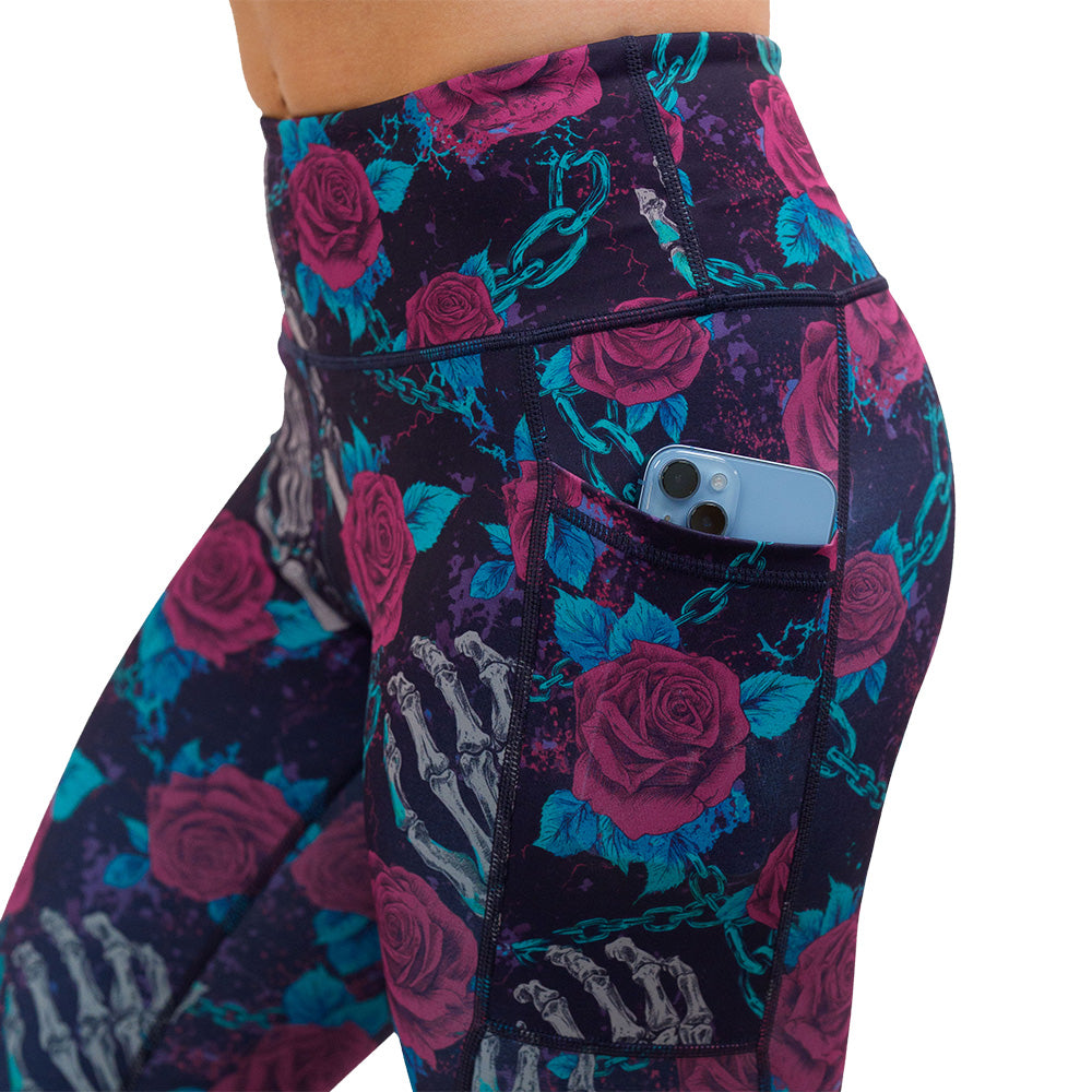 close up of the roses and skeleton hands connected by chain links pattern leggings with a phone in the pocket against a white background