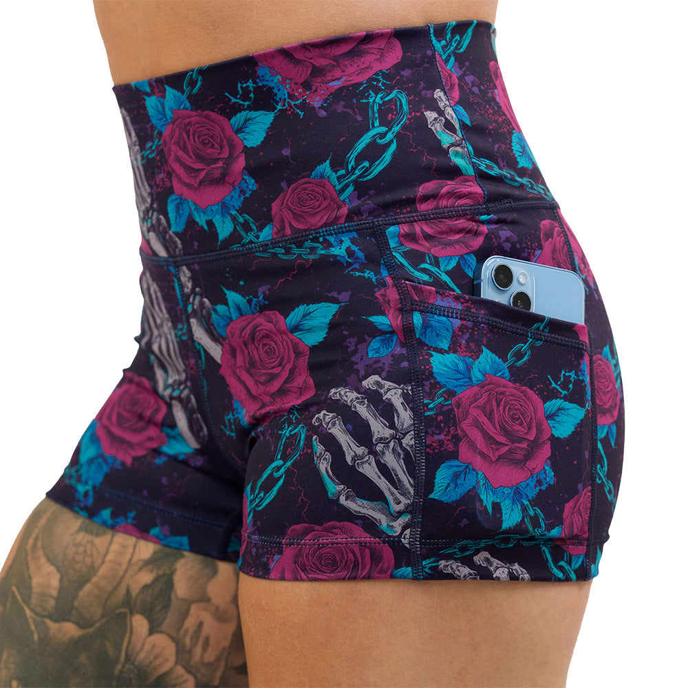 close up of the roses and skeleton hands connected by chain links pattern 2.5 inch shorts with a phone in the pocket against a white background