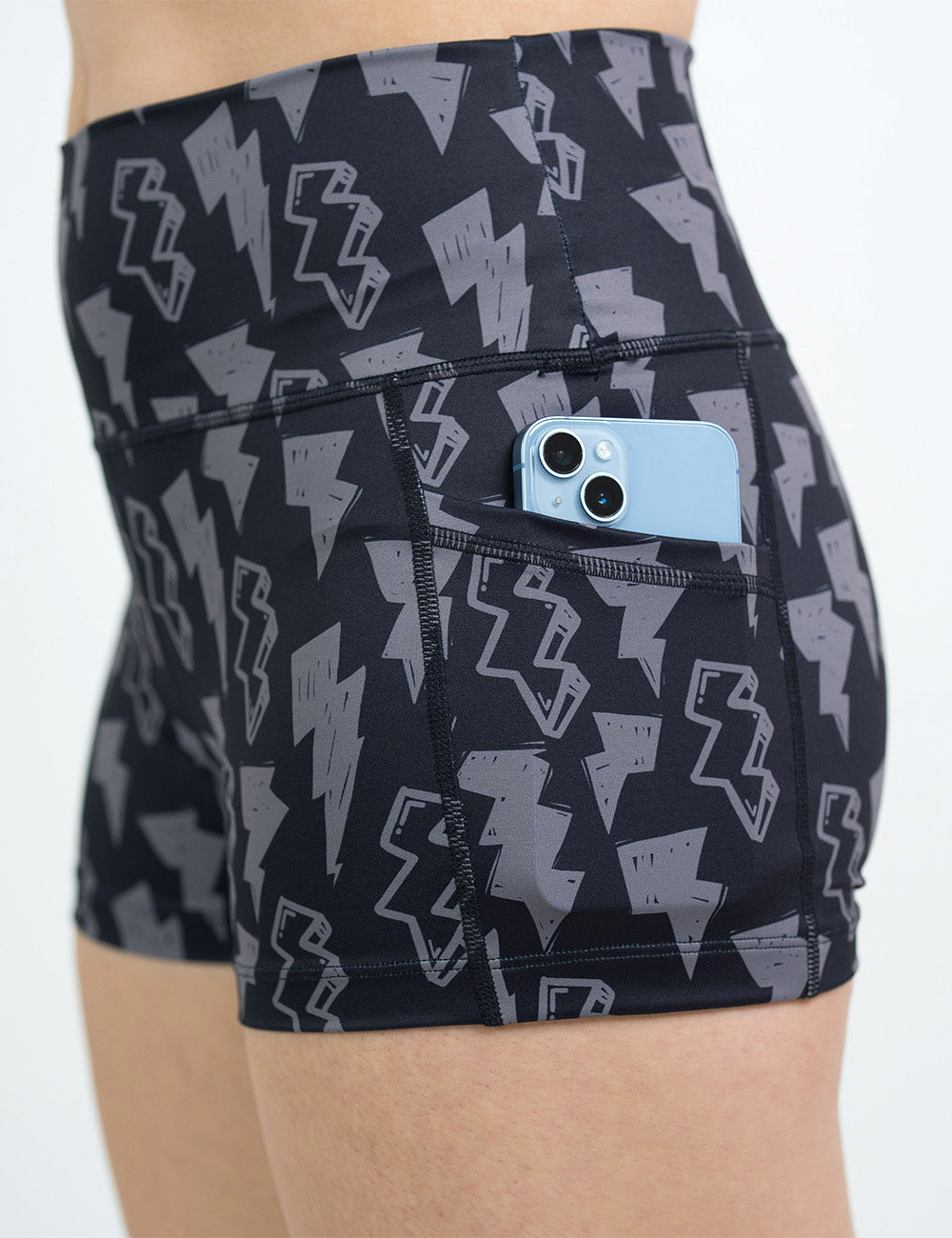 close up of the 2.5 inch black shorts with grey lightning bolts with a phone in its pocket against a white background