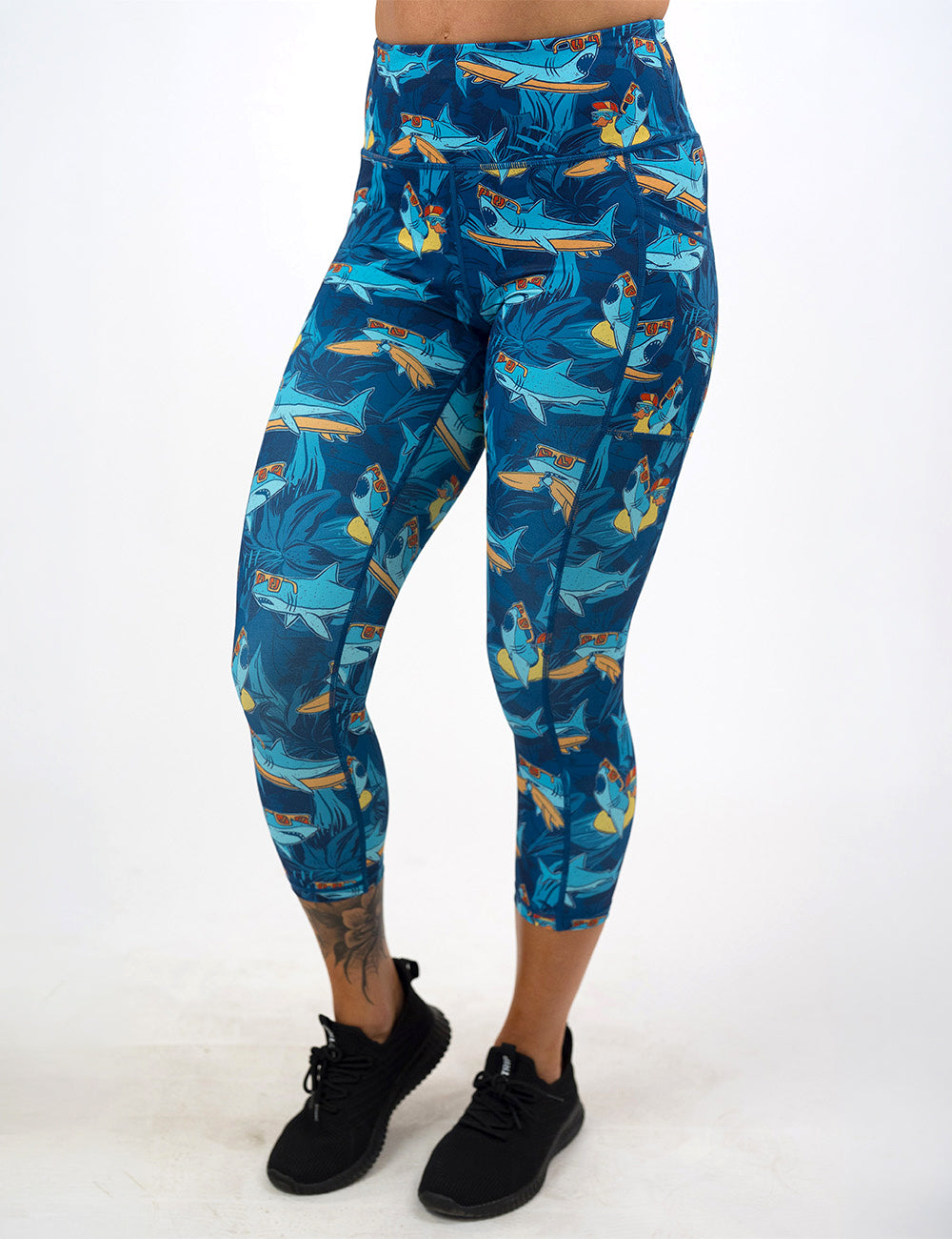front of the capri cartoon sharks surfboarding with sunglasses leggings against a white background