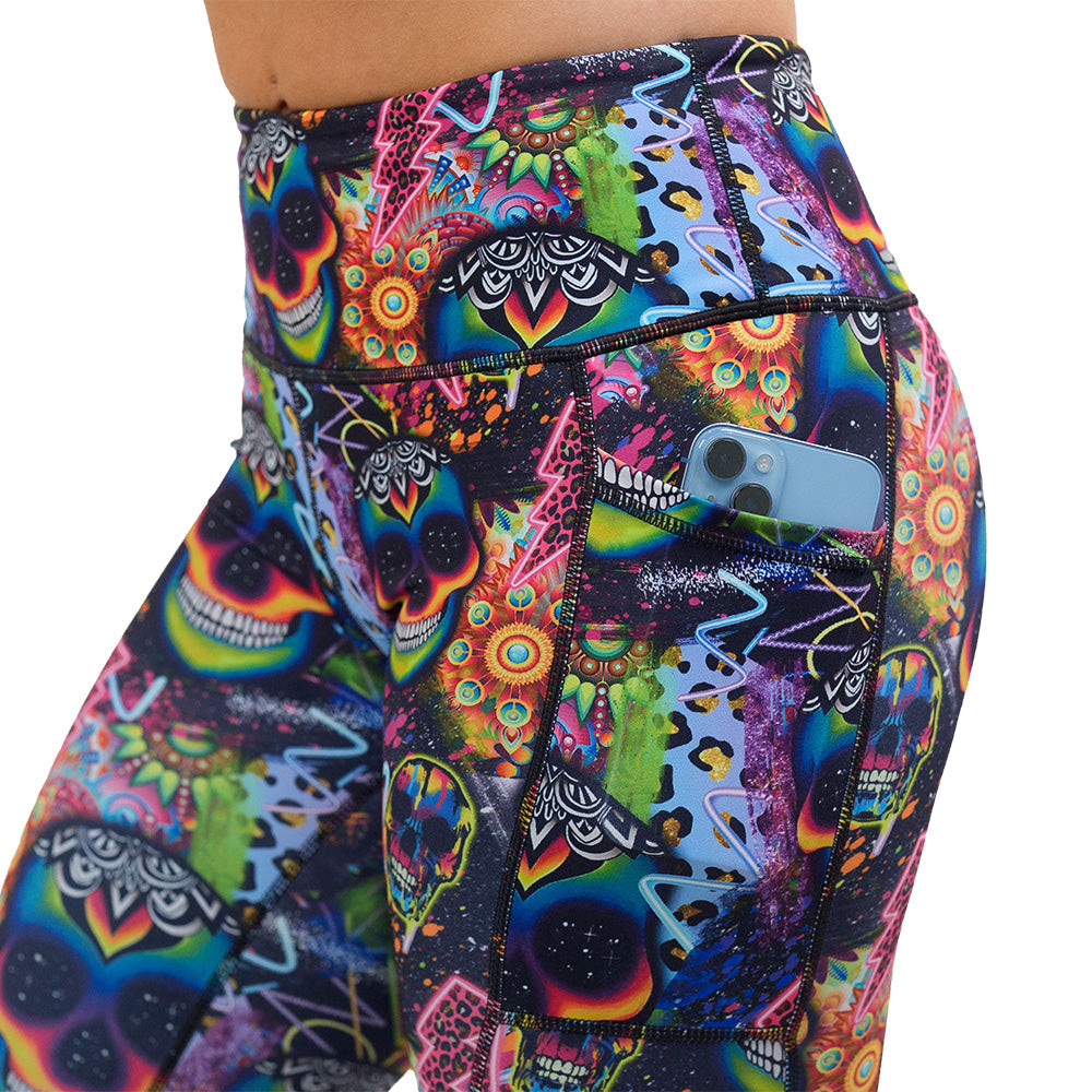 close up of the brightly colored psychedelic skulls pattern against a busy background full of designs leggings with a phone in its pocket against a white background
