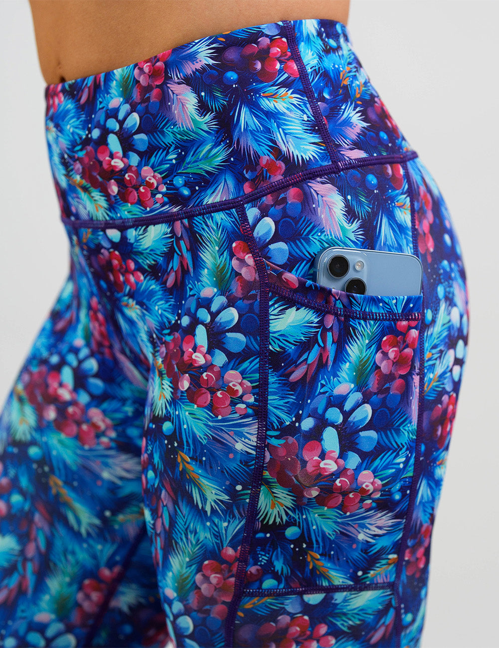 close up of the winter berries among blue leaves leggings with a phone in its pocket