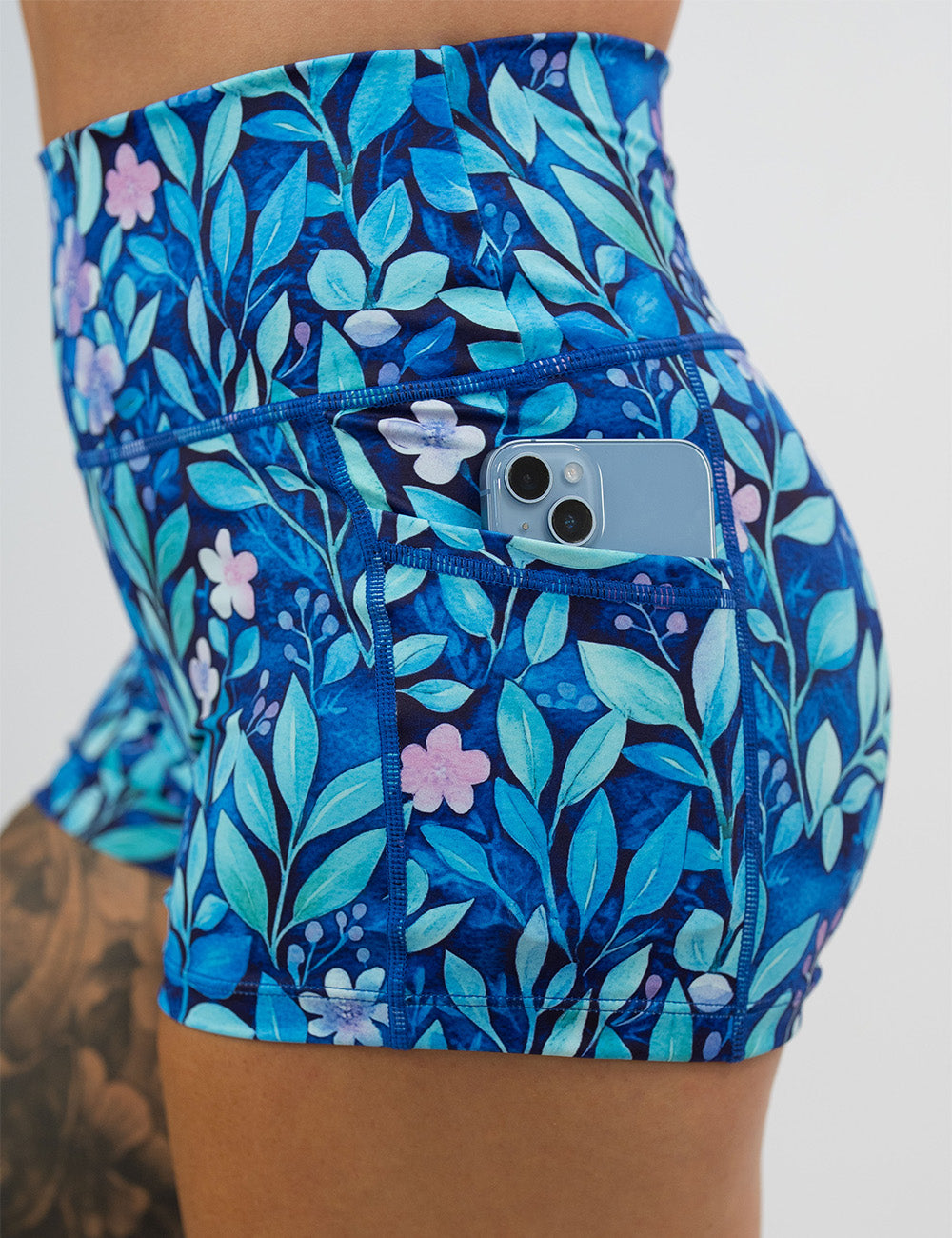 close up of the 2.5 inch blue flowers and vines shorts pockets holding a phone against a white background