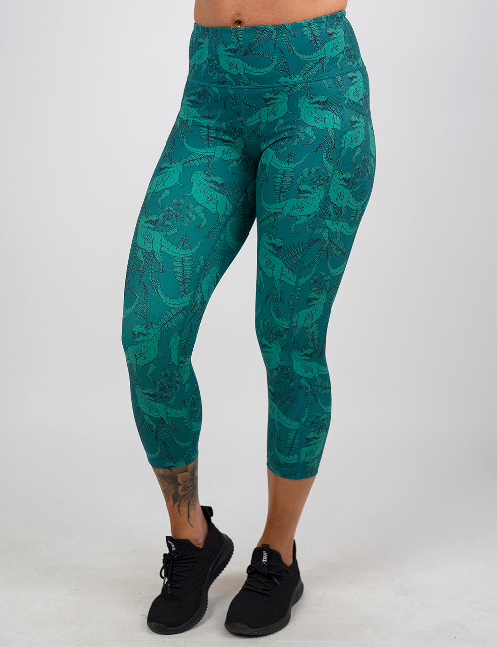 front of the teal t-rex pattern capri leggings against a white background