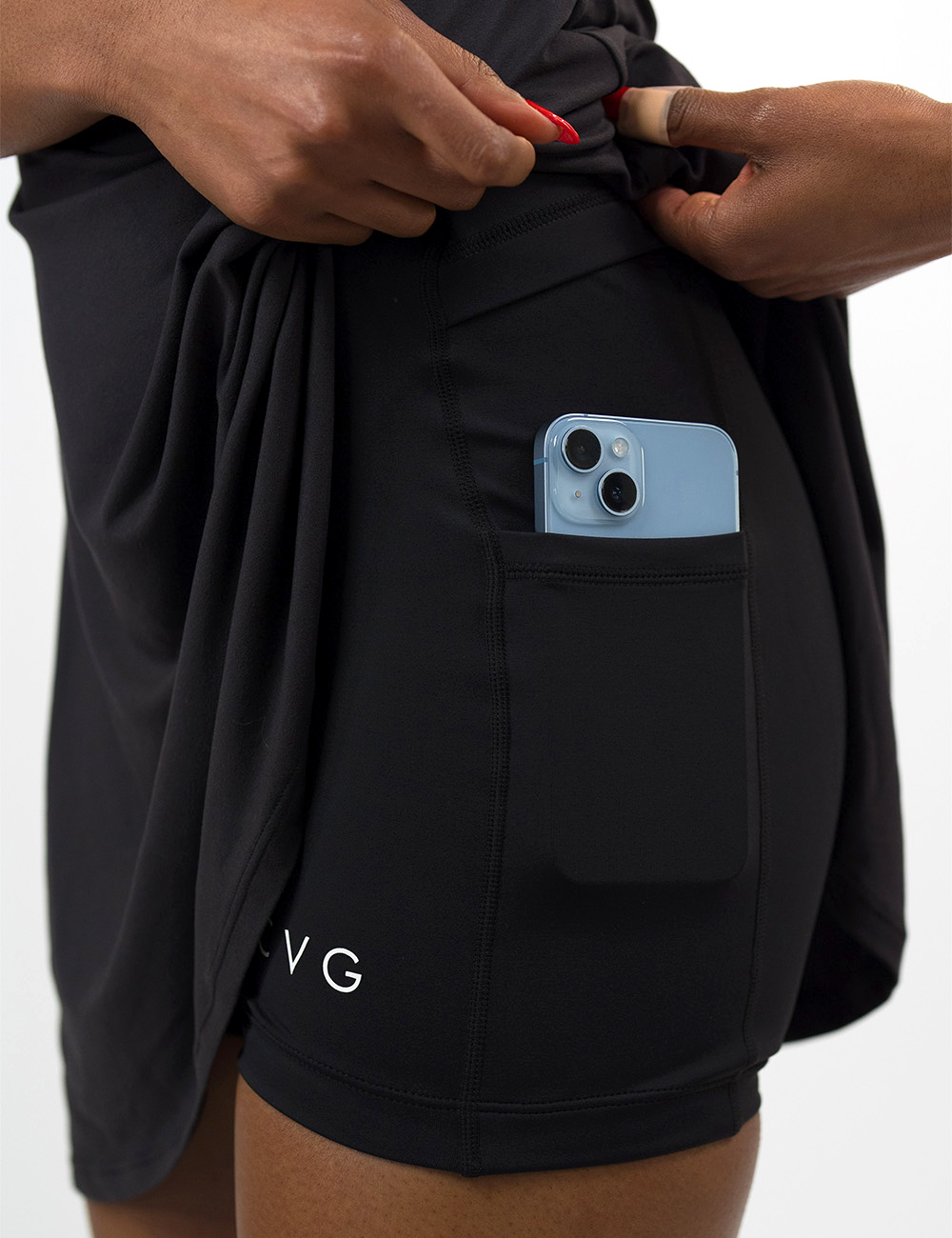 close up of the black activewear dress pulled up to show the shorts underneath with a phone in the pocket against a white background