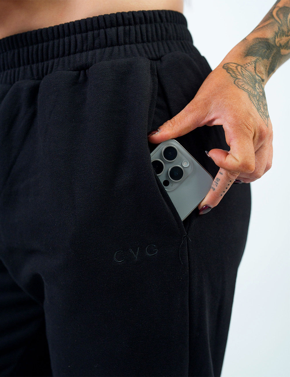 close up of the black sweat pants with a subtle cvg logo with a phone in its pocket